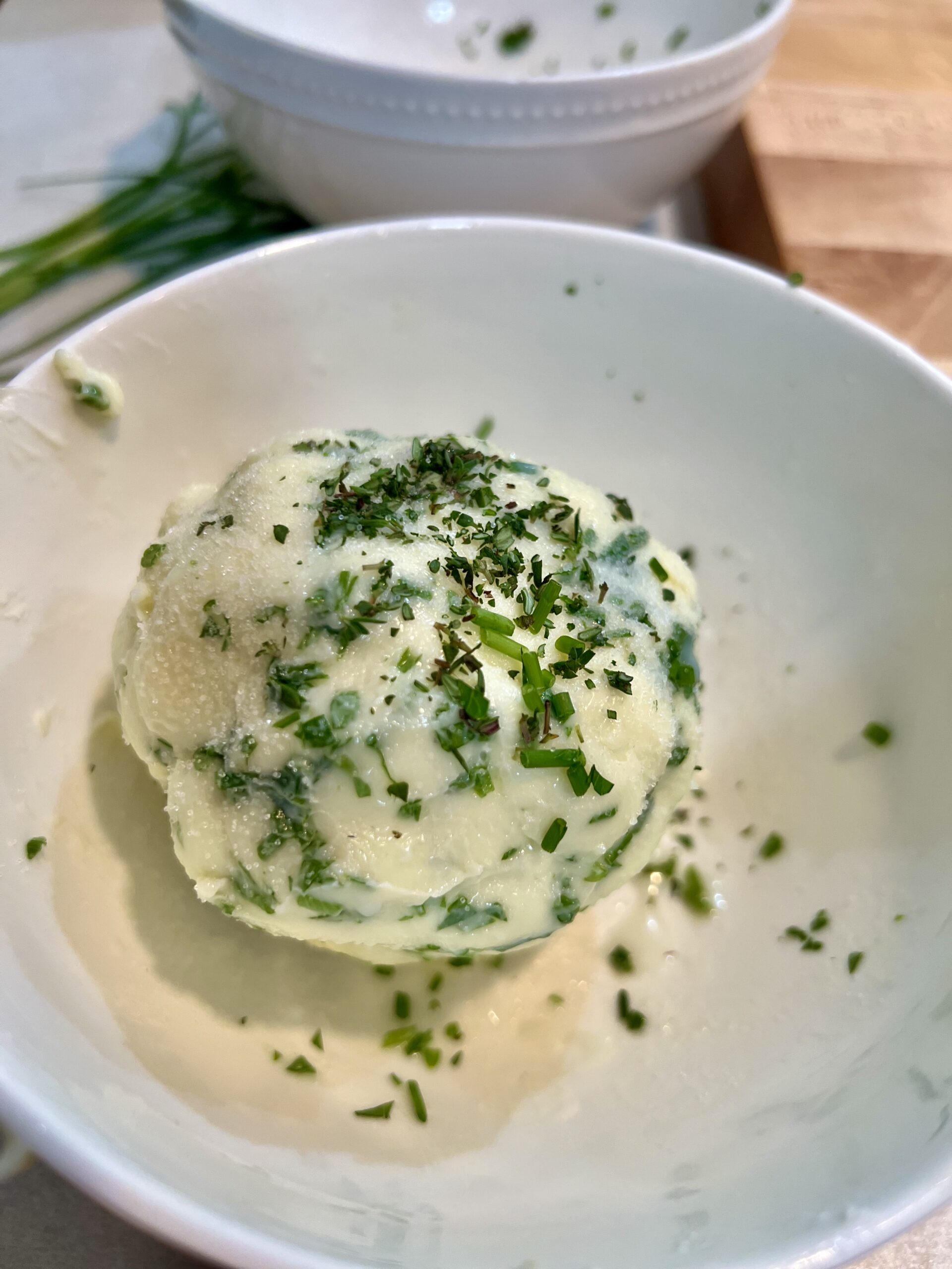 Ball of homemade herb butter in a white bowl on the counter