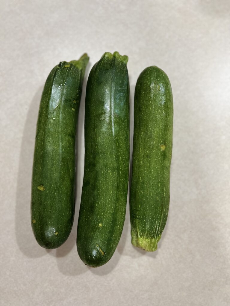 Three small size zucchinis laying on a white counter top