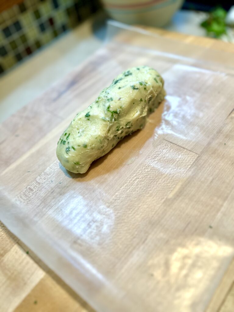 Homemade herb butter sitting on wax paper on top of a wooden cutting board