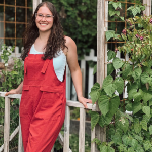 girl wearing red overalls standing again her wooden garden fence