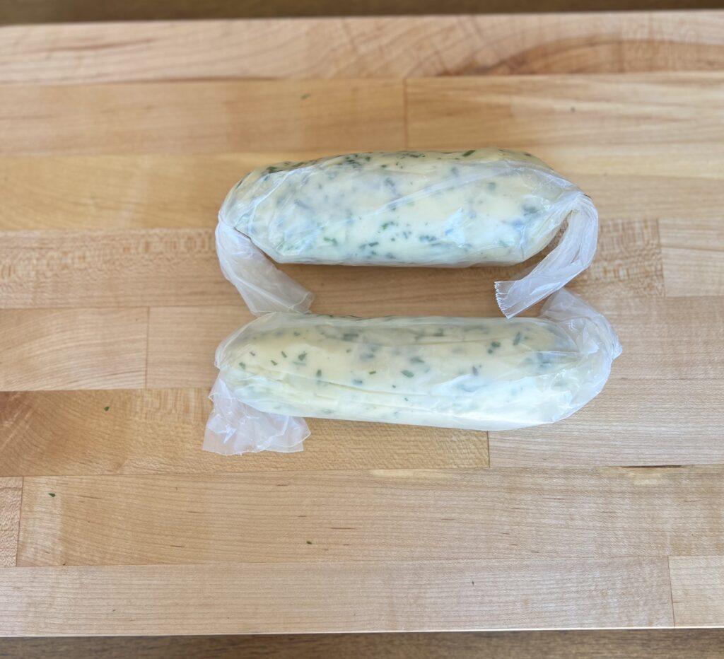 wrapped herb butter in wax paper on top of a wood cutting board