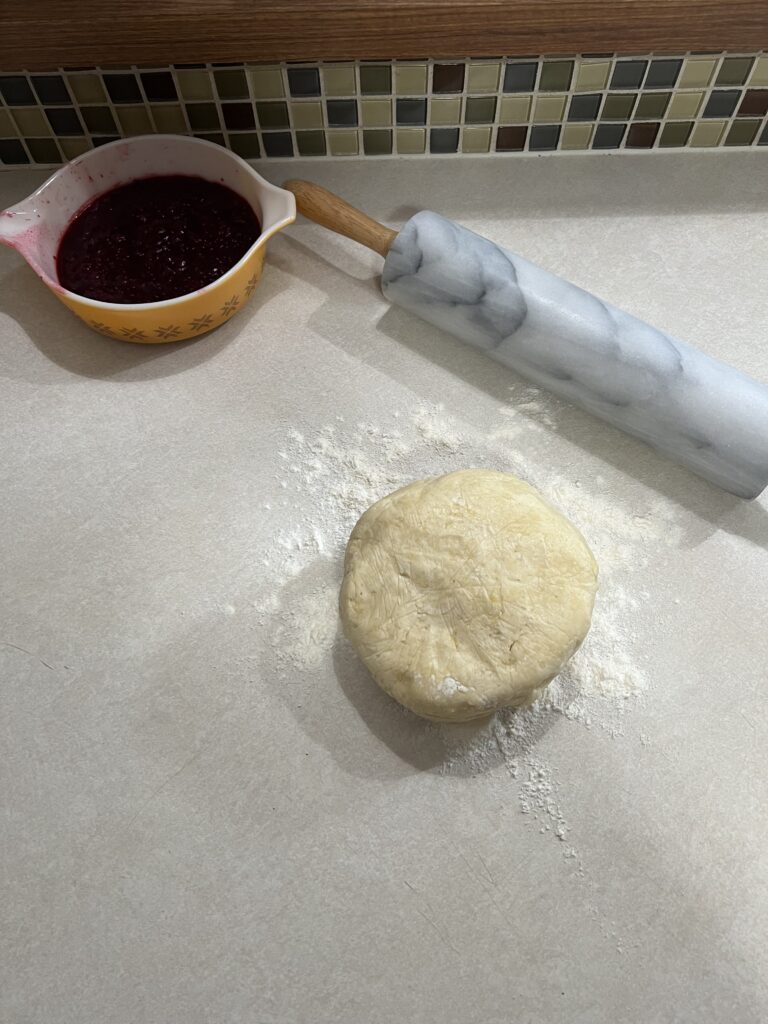 Sourdough discard pastry dough sitting on a lightly floured counter with jam and rolling pin next to it