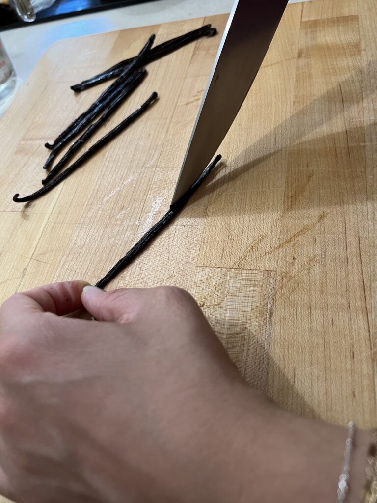 A girl using a sharp knife to cut open a vanilla bean.