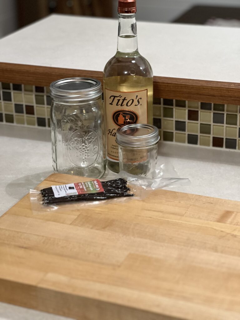 Two mason jars, vanilla bean and vodka sitting on a white counter