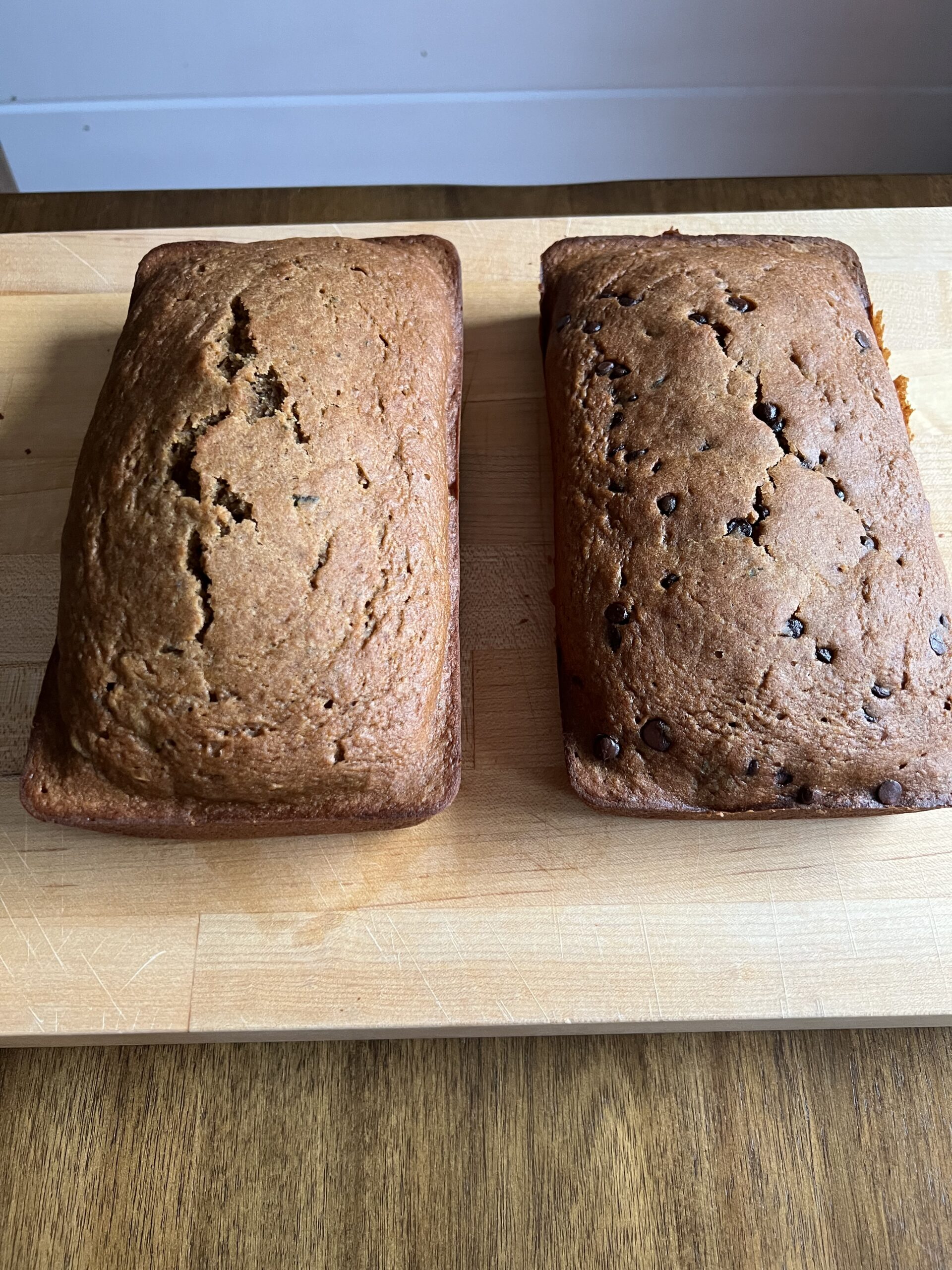 two loafs of pumpkin zucchini bread sitting on a wooden cutting board